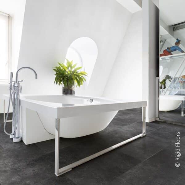 Salle de bain minimaliste : baignoire îlot blanche et robinetterie chromée sur sol texturé foncé. Lumière naturelle sur murs inclinés.