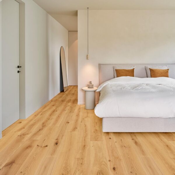 Intérieur de chambre minimaliste: grand lit beige, murs clairs, et parquet en chêne doré. Un couloir mène à un miroir ovale.