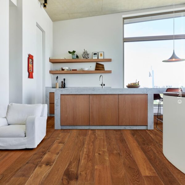 Intérieur moderne baigné de lumière, montrant un grand plancher de bois franc brun-roux. L'îlot de cuisine combine marbre gris et bois, sous un plafond en béton brut.