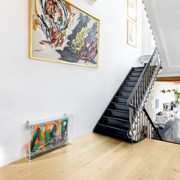 Hall d'entrée lumineux avec parquet clair et escalier noir. Grande toile abstraite signée K. Appel '58 au-dessus d'une sculpture cinétique.