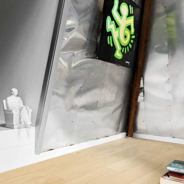 Tableau K. Haring sur mur aluminium froissé. À gauche, sculpture blanche assise. Plancher en chêne clair. Ambiance industrielle chic.