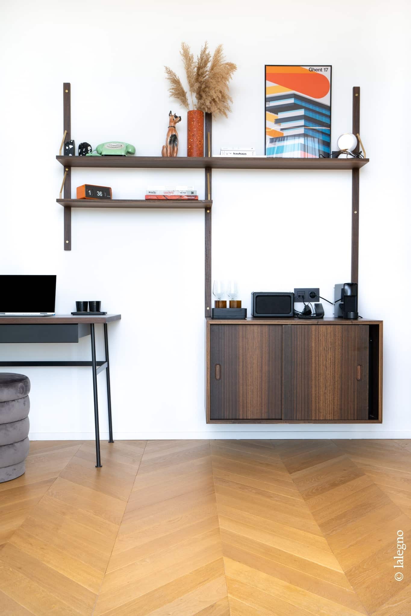 Rangement mural en bois foncé style mid-century avec étagères et meuble bas. Décor rétro (horloge 1:36, poster Ghent 17). Bureau et parquet chevron.