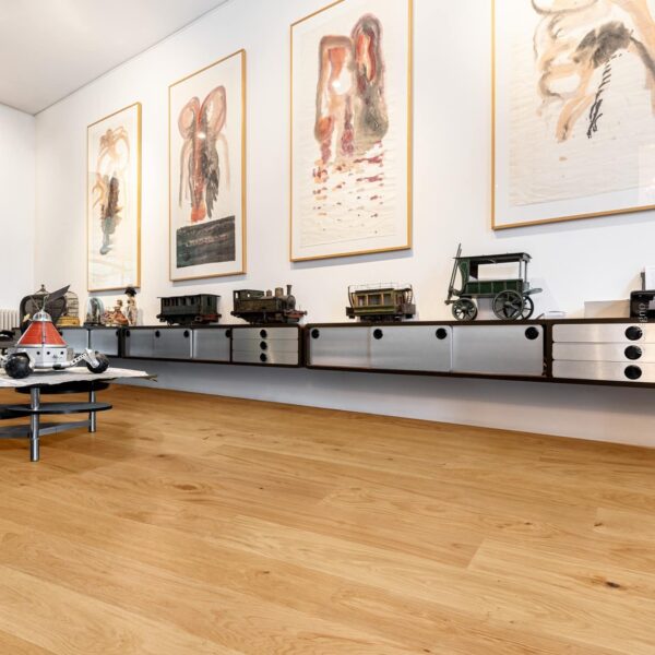 Parquet en chêne clair chaleureux dans une galerie. Meuble design flottant supportant des trains miniatures anciens et grands tableaux abstraits.