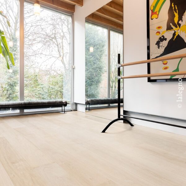 Parquet chêne clair dans un studio de danse lumineux. Grandes fenêtres, plafond poutres bois, barre de ballet, et miroir mural.