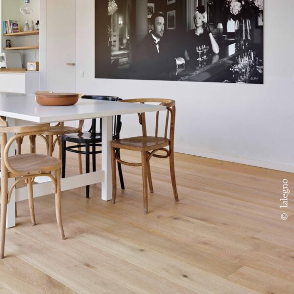 Parquet chêne clair à larges planches. Salle à manger moderne avec table blanche et chaises bistrot. Grande photo noir et blanc chic au mur.