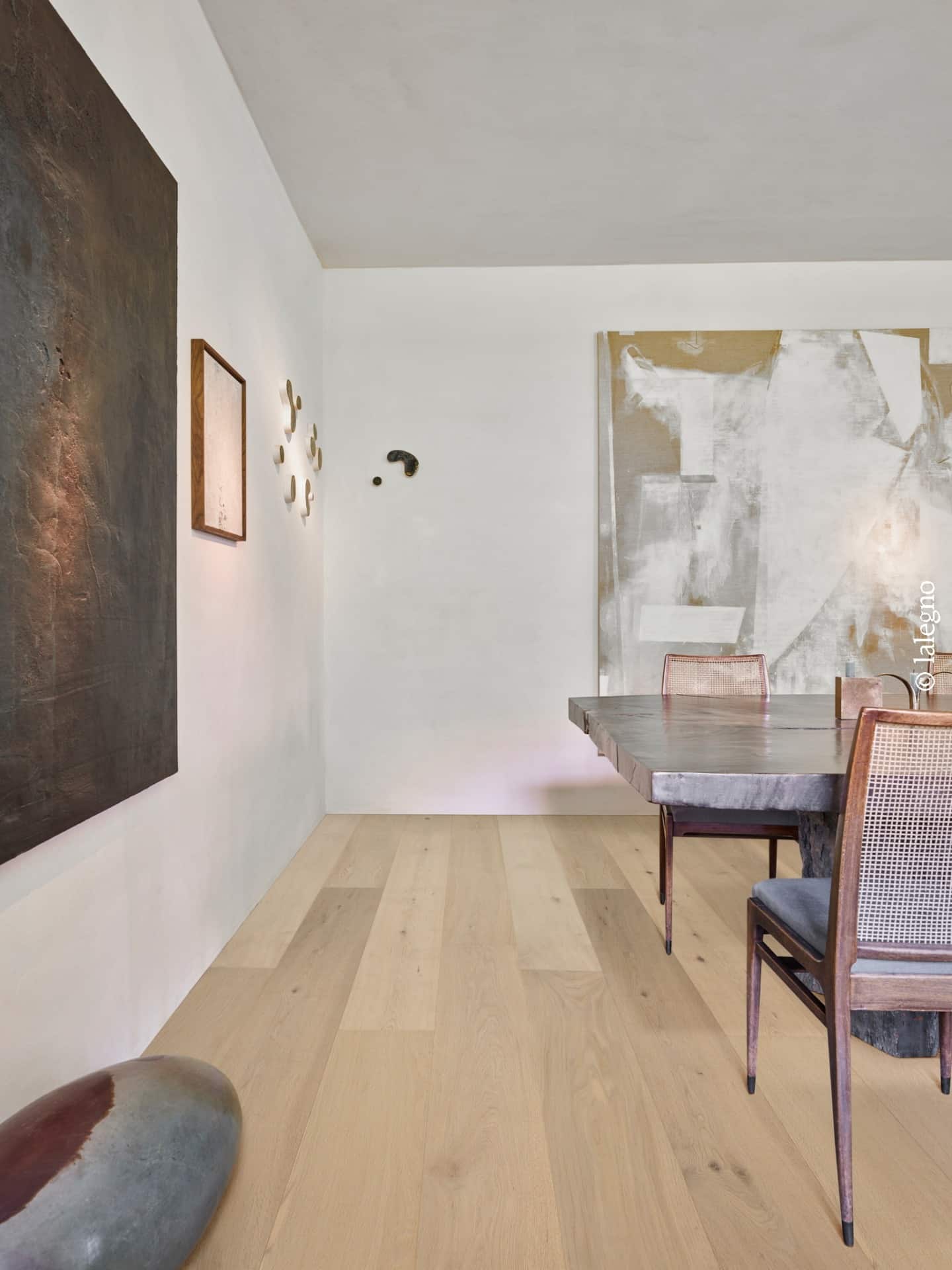 Parquet chêne clair naturel Lalegno dans salle à manger minimaliste. Table en bois brut, chaises cannées et grands tableaux d'art abstrait.