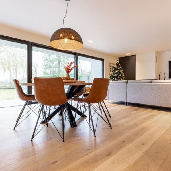Parquet chêne clair dans salon moderne avec table à manger ronde, chaises industrielles en cuir et grand canapé gris près d'une baie vitrée.