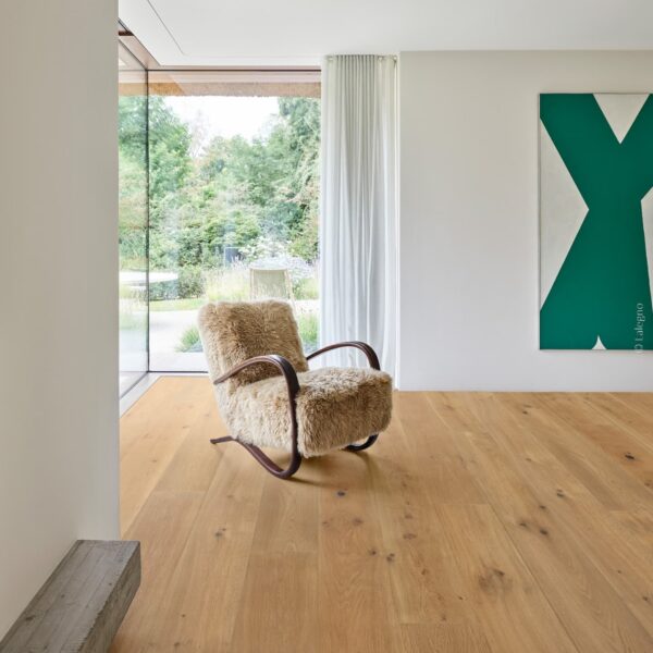 Fauteuil en fourrure devant une baie vitrée sur jardin. Plancher chêne naturel. Mur blanc, tableau vert abstrait.