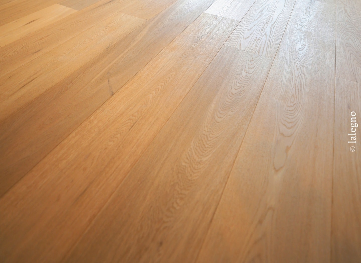Gros plan sur un parquet en chêne clair. Lames larges et grain apparent mises en valeur par une lumière naturelle. © lalegno.