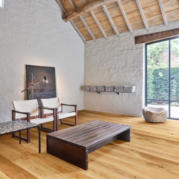 Loft design rustique aux murs de briques blanches et poutres apparentes. Parquet en chêne clair, mobilier sombre et baies vitrées.