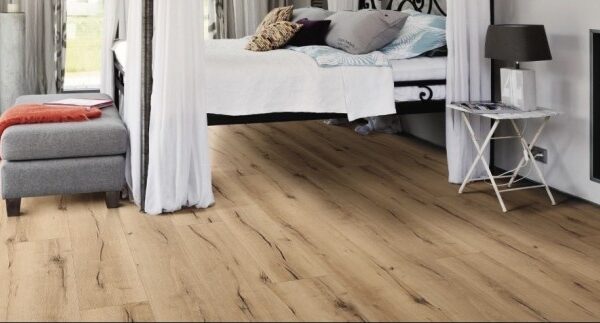 Parquet chêne naturel à planches larges, posé dans une chambre au style rustique-chic. Lit surélevé, pouf gris et cheminée décorative.