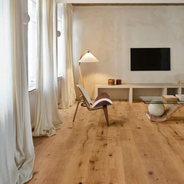 Salon moderne minimaliste avec large parquet en chêne naturel. Fauteuil design, console basse, et longs rideaux en lin clairs.