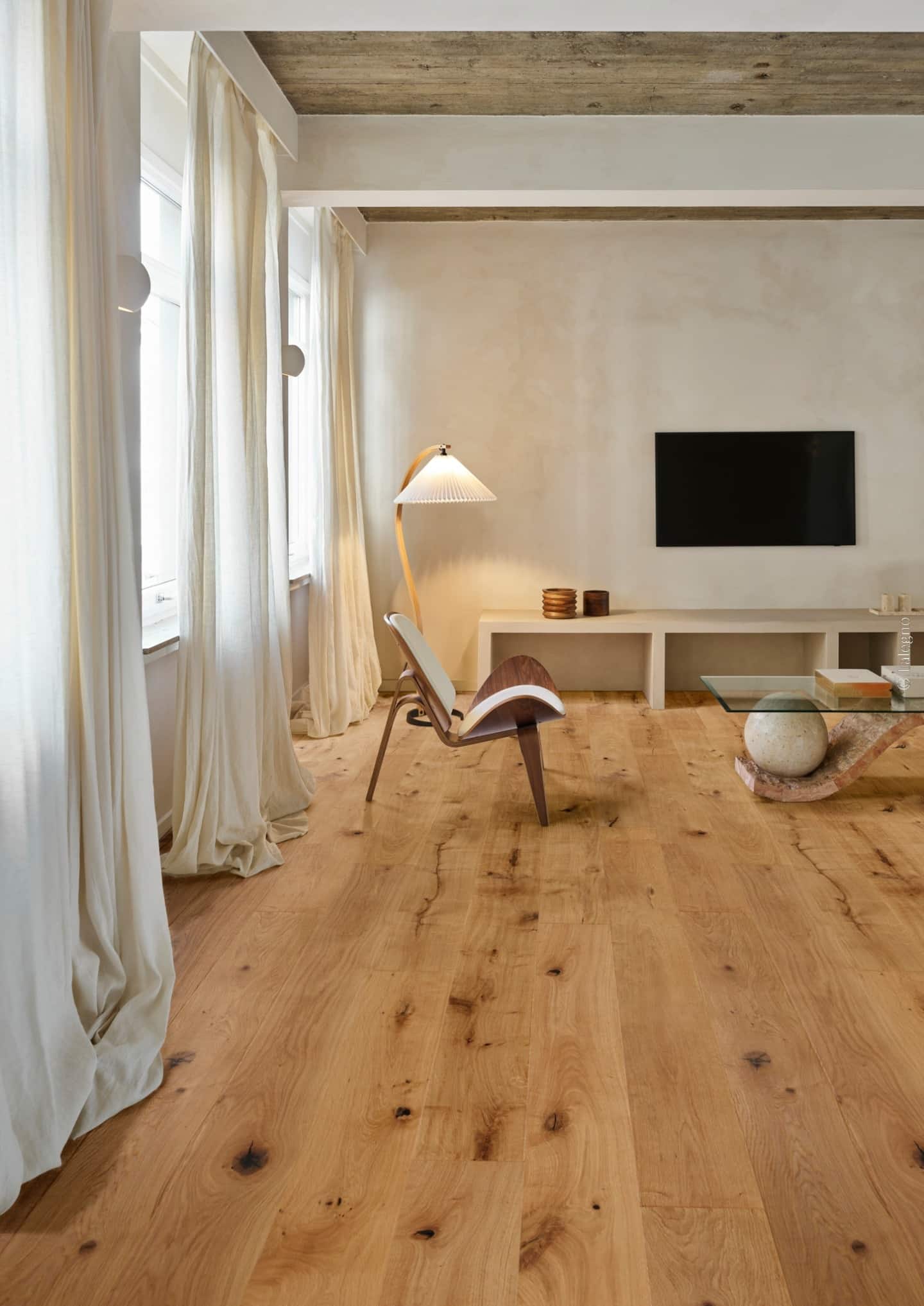 Salon moderne minimaliste avec large parquet en chêne naturel. Fauteuil design, console basse, et longs rideaux en lin clairs.