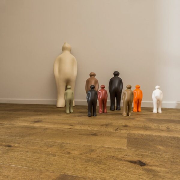 Collection de figurines décoratives colorées devant une sculpture géante beige, sur un sol bois rustique (parquet) (© lalegno).