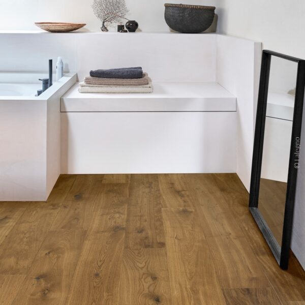 Salle de bain mansardée moderne avec parquet en chêne brun. Banquette blanche intégrant une baignoire et des serviettes. Poutre apparente.
