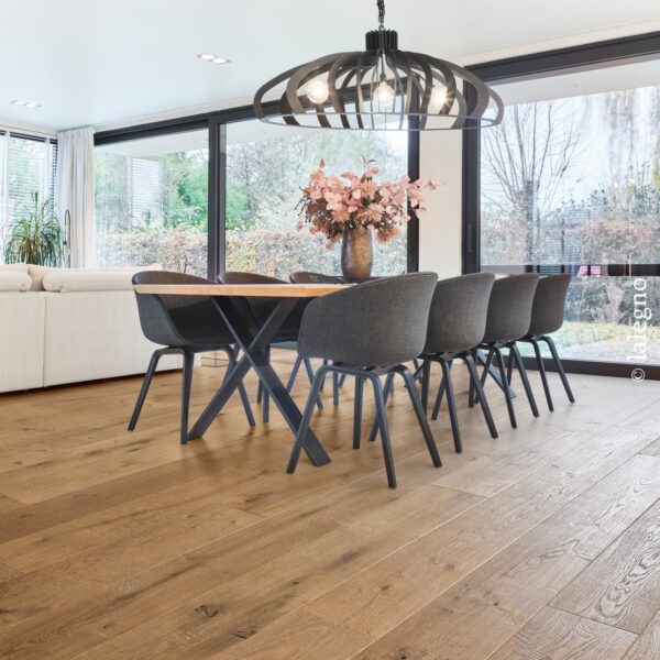 Salle à manger moderne baignée de lumière naturelle. Plancher chêne à larges lames, table en bois et chaises grises.