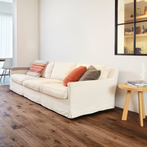 Grand canapé blanc cassé dans un salon moderne. Parquet en noyer riche et sombre. Logo ©lalegno visible.