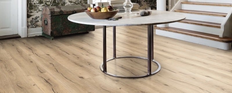 Plancher à lattes de bois clair au grain rustique. Il équipe une entrée meublée d'une table ronde en marbre et d'un coffre vintage.