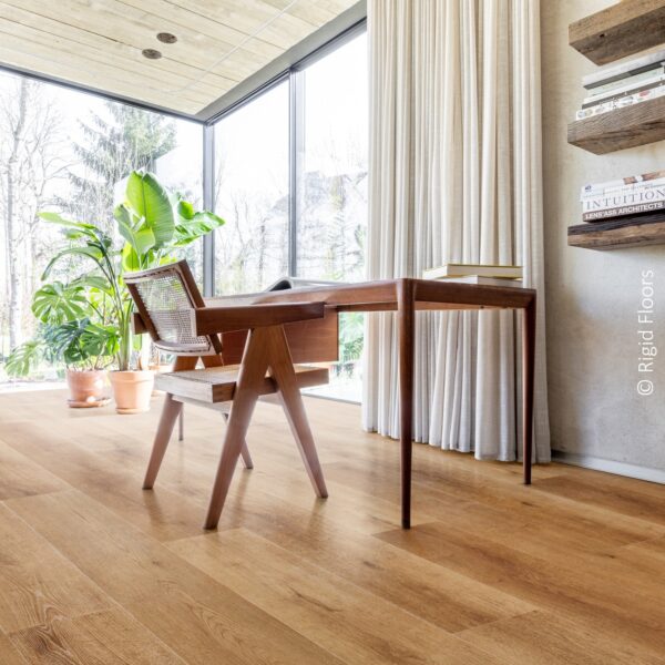 Plancher chêne clair Rigid Floors dans un espace lumineux. Grand bureau bois, chaise cannage, murs béton et rideaux.