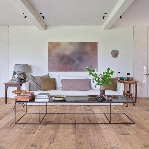 Salon design minimaliste : canapé blanc, grande œuvre abstraite et table basse moderne sur plancher en bois naturel.