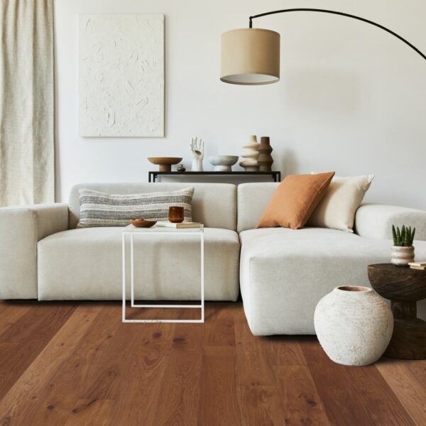 Salon minimaliste avec grand canapé modulaire beige, sol en parquet bois foncé, et décoration aux tons neutres terre cuite.