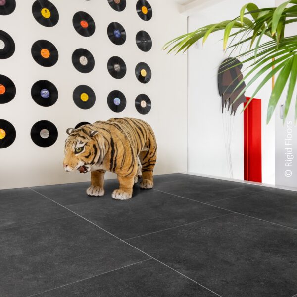 Grand sol carrelé noir, intérieur moderne et éclectique. Un tigre en peluche devant un mur décoré de disques vinyles.