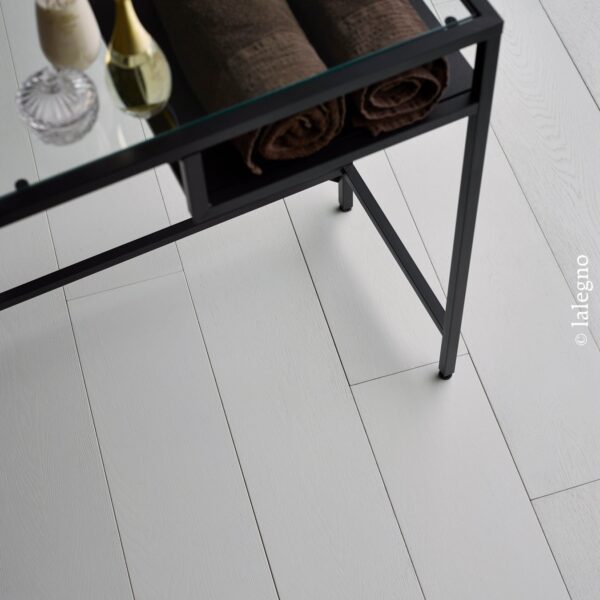 Parquet bois clair blanchi (chêne) sous une table en métal noir. La tablette supporte des serviettes spa marron et des flacons élégants.